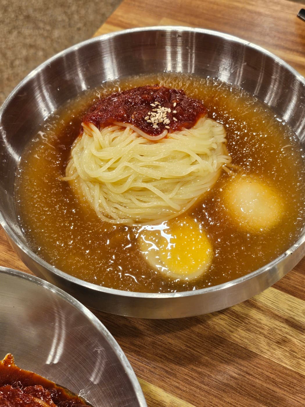 A bowl of milmyeon with cold broth and red sauce on a metal table