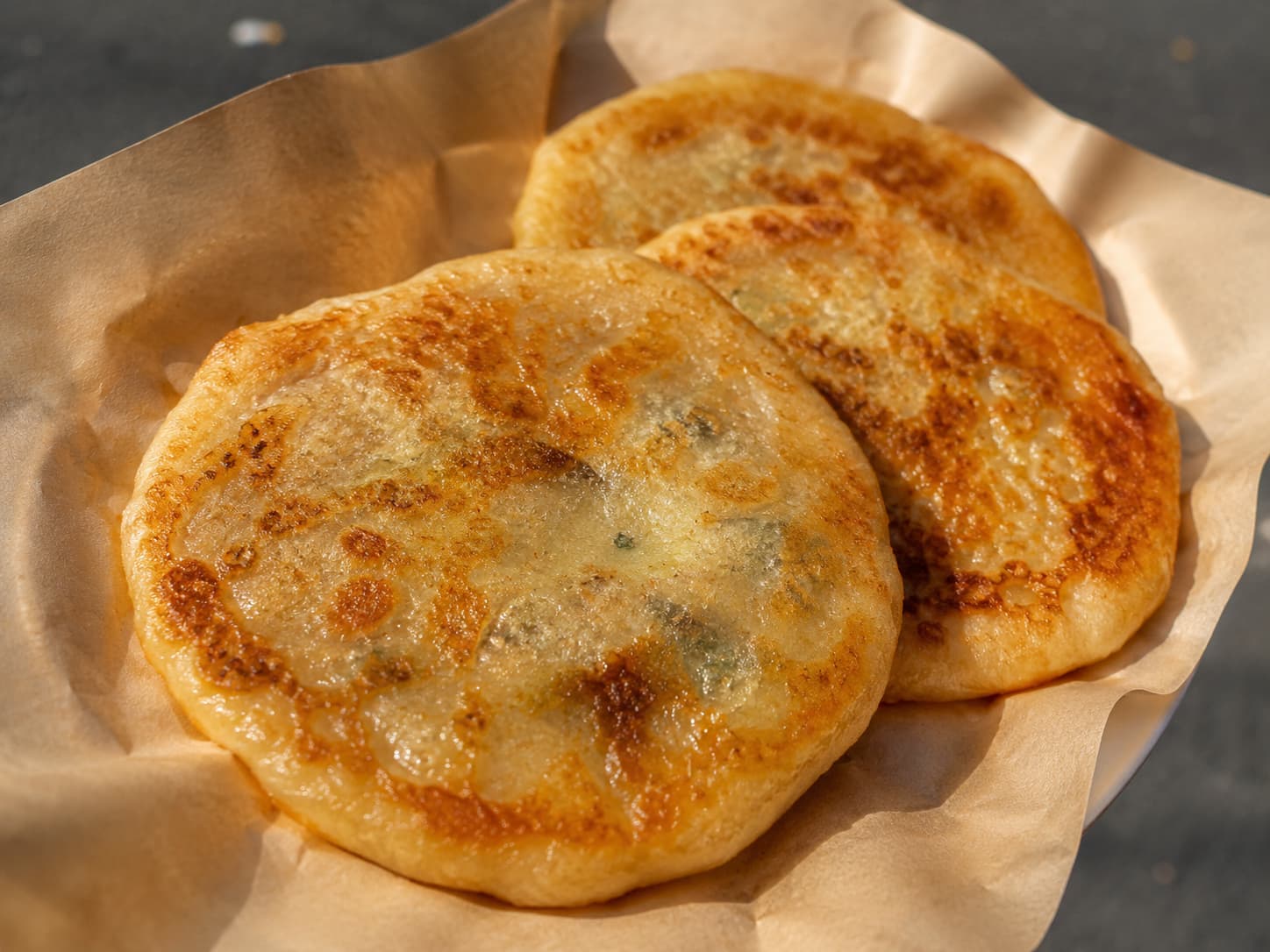 Two whole, golden-brown hotteok served on a piece of paper wrapping.